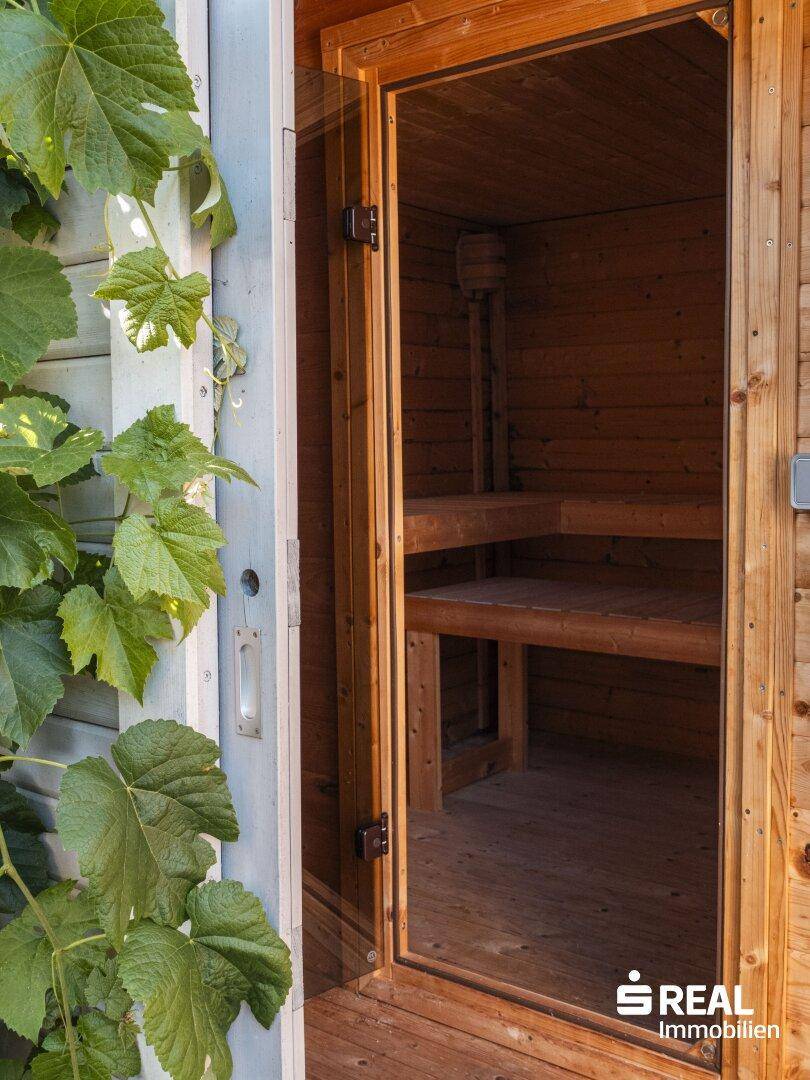 Eingangsbereich einer Holzsauna im Freien, umgeben von grünen Pflanzen.