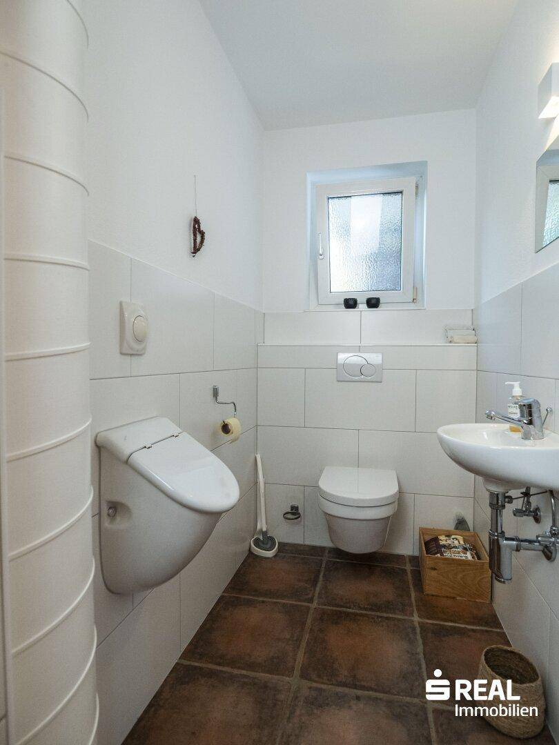 Modernes Gäste-WC mit Urinal, wandhängendem WC, Waschbecken und Fenster.