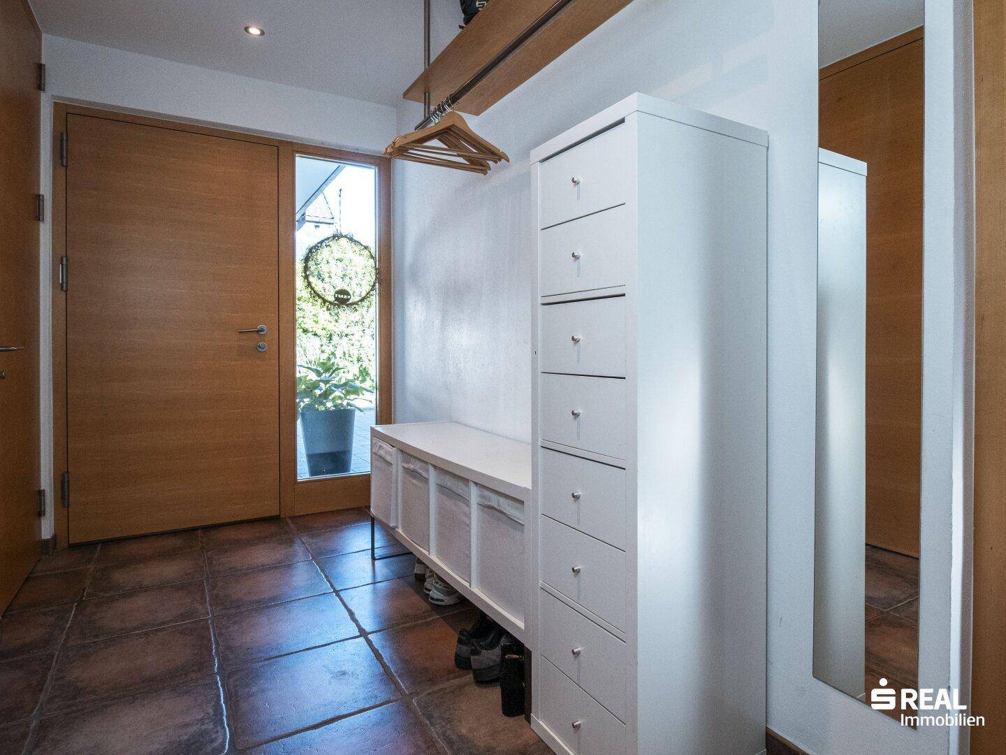 Heller Eingangsbereich mit Terrakotta-Fliesenboden, Garderobe und großem Spiegel.