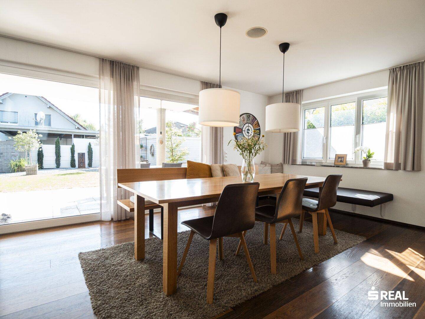 Geräumiger Essbereich mit Holztisch, Sitzbank und Zugang zum Garten durch große Fenster.