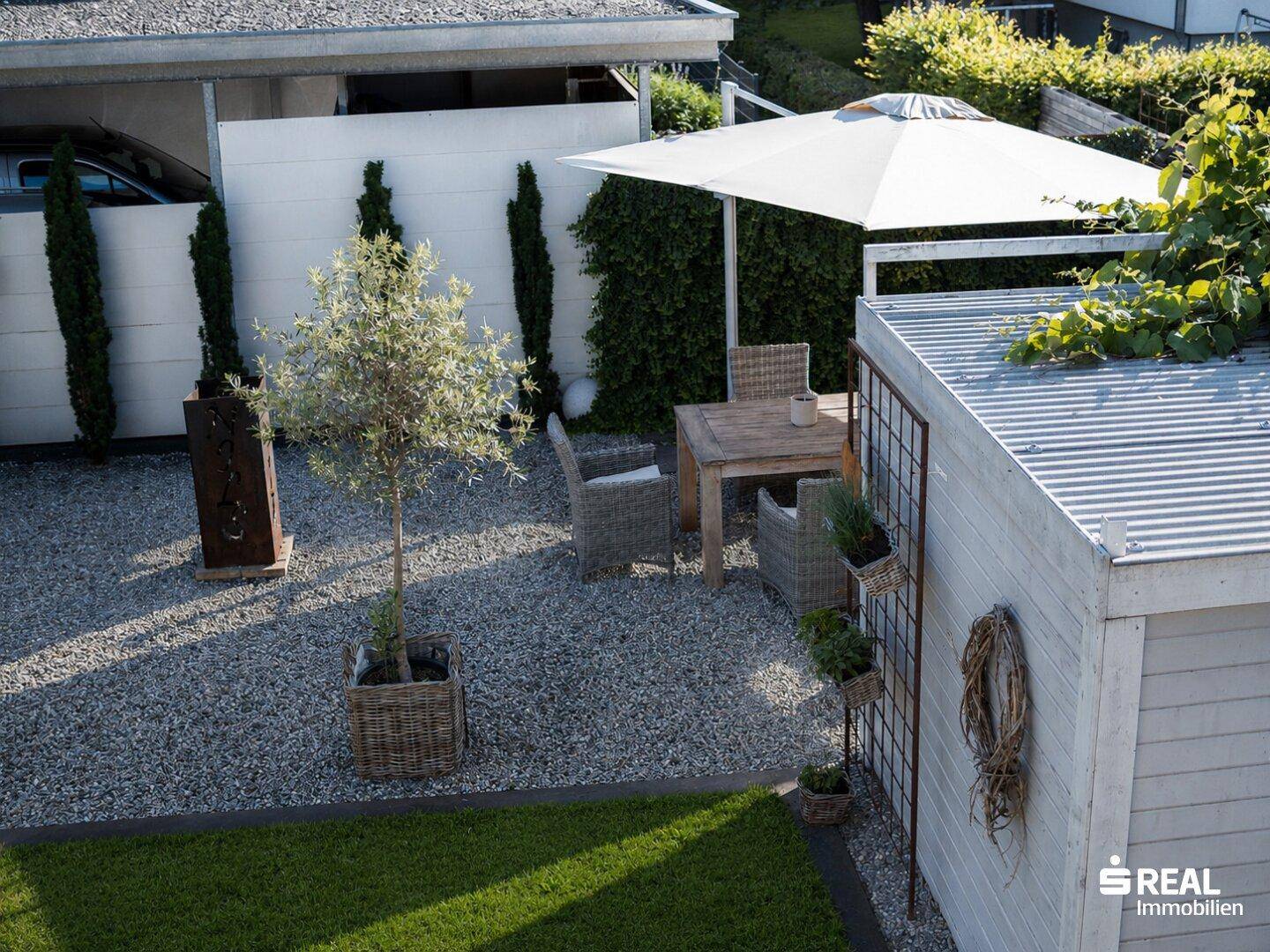 Gemütlicher Sitzbereich im Kiesgarten mit Sonnenschirm, Gartenmöbeln und mediterraner Bepflanzung.