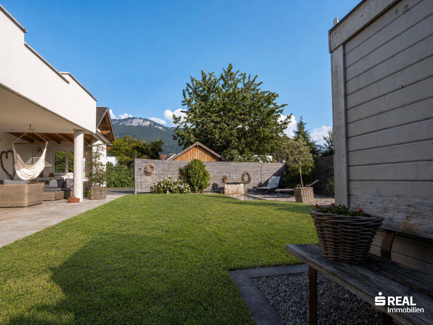 Sonniger Garten mit Rasenfläche, Terrasse und malerischem Bergblick im Hintergrund.