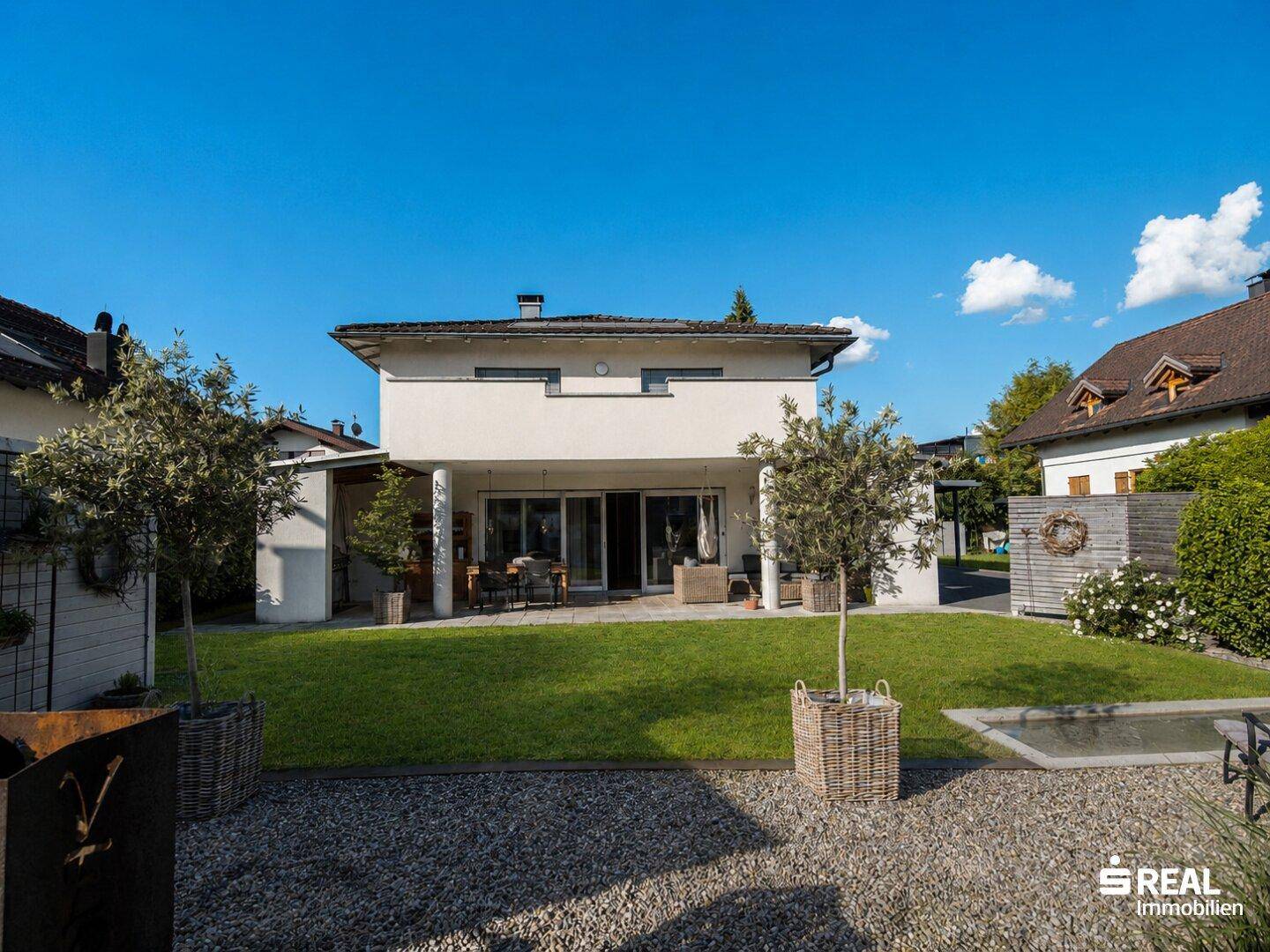 Rückansicht eines modernen Einfamilienhauses mit großer Rasenfläche und Terrasse.