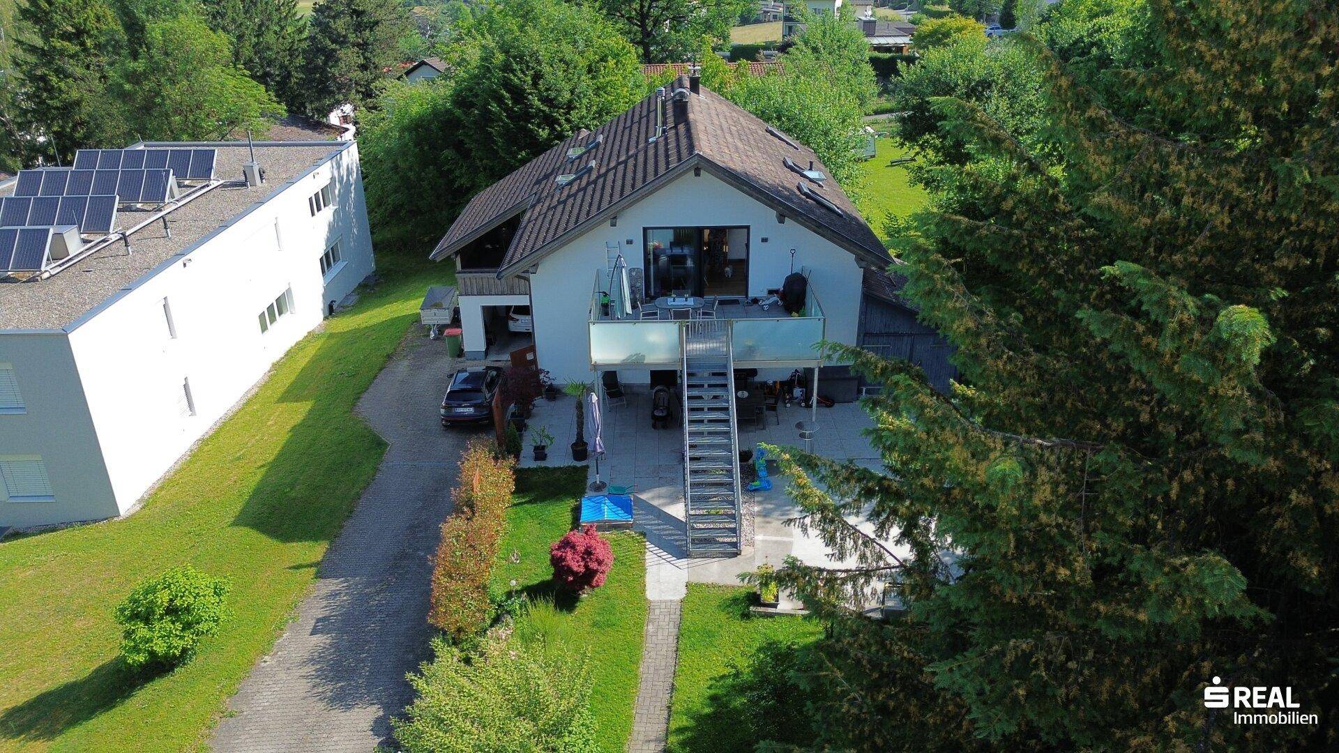 Luftaufnahme des Hauses mit Garten, Balkonen und einem Nachbargebäude mit Solaranlage.