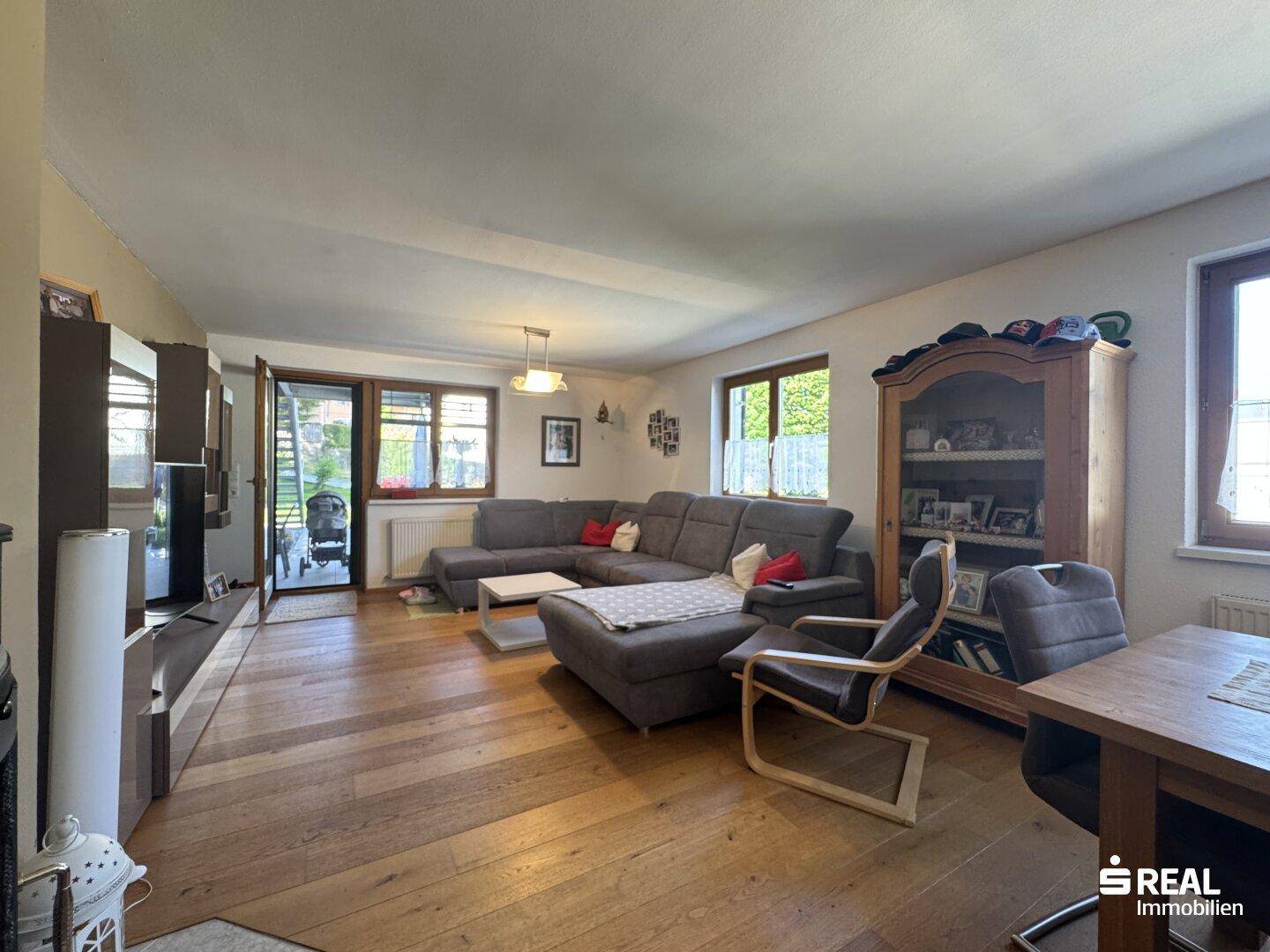 Geräumiger Wohn-Essbereich mit Holzboden, großem Sofa und Zugang zur Terrasse.
