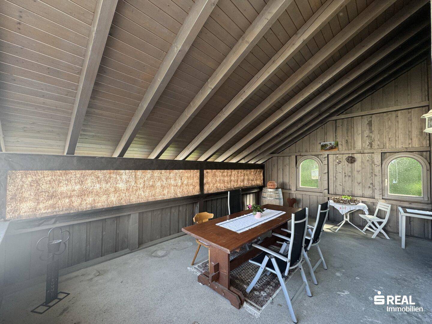 Rustikale Loggia mit Holztisch und Stühlen, umgeben von Holzwänden und -decke.