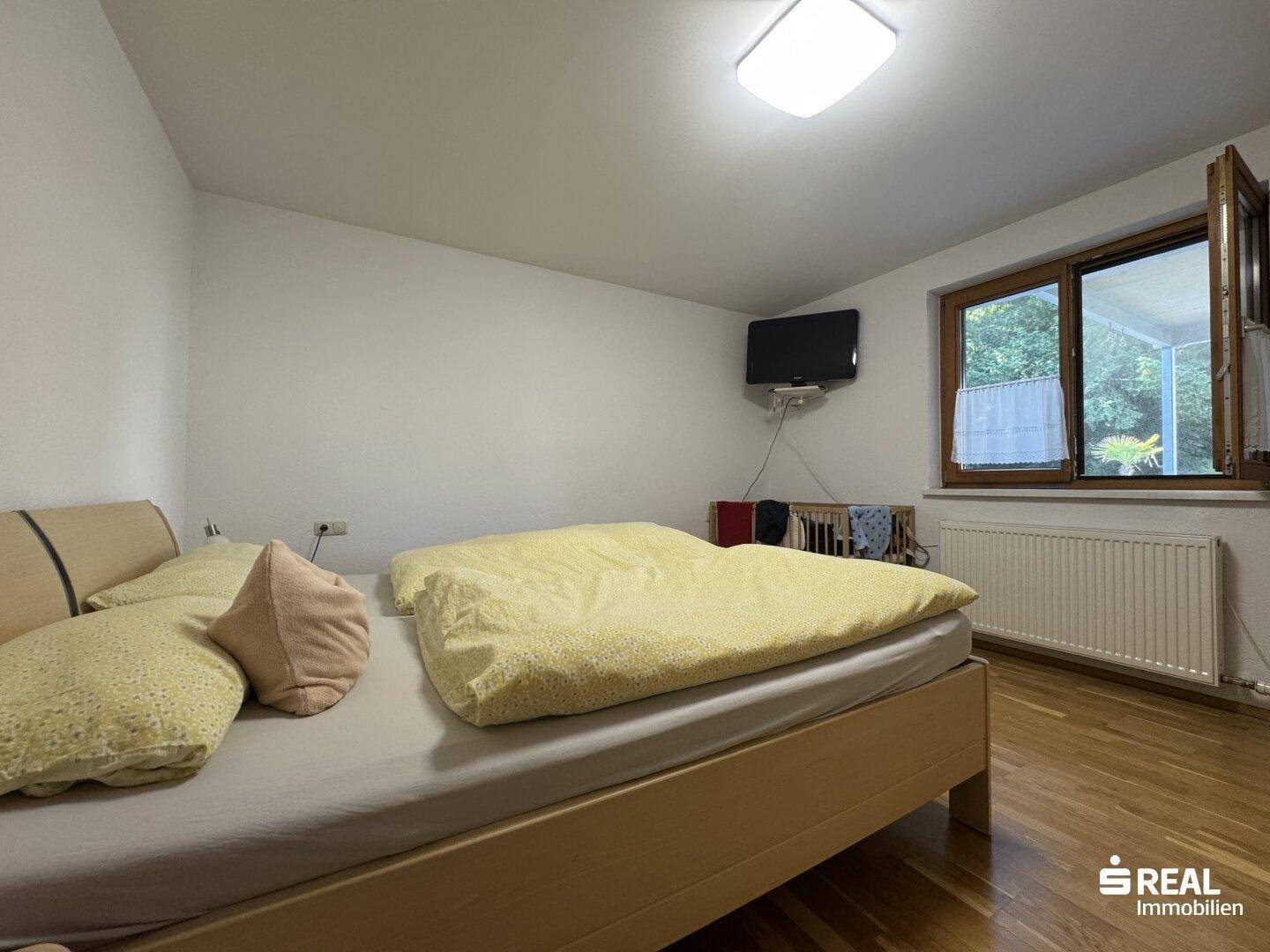 Schlafzimmer mit Holzboden, Doppelbett und Fenster mit Blick ins Grüne.