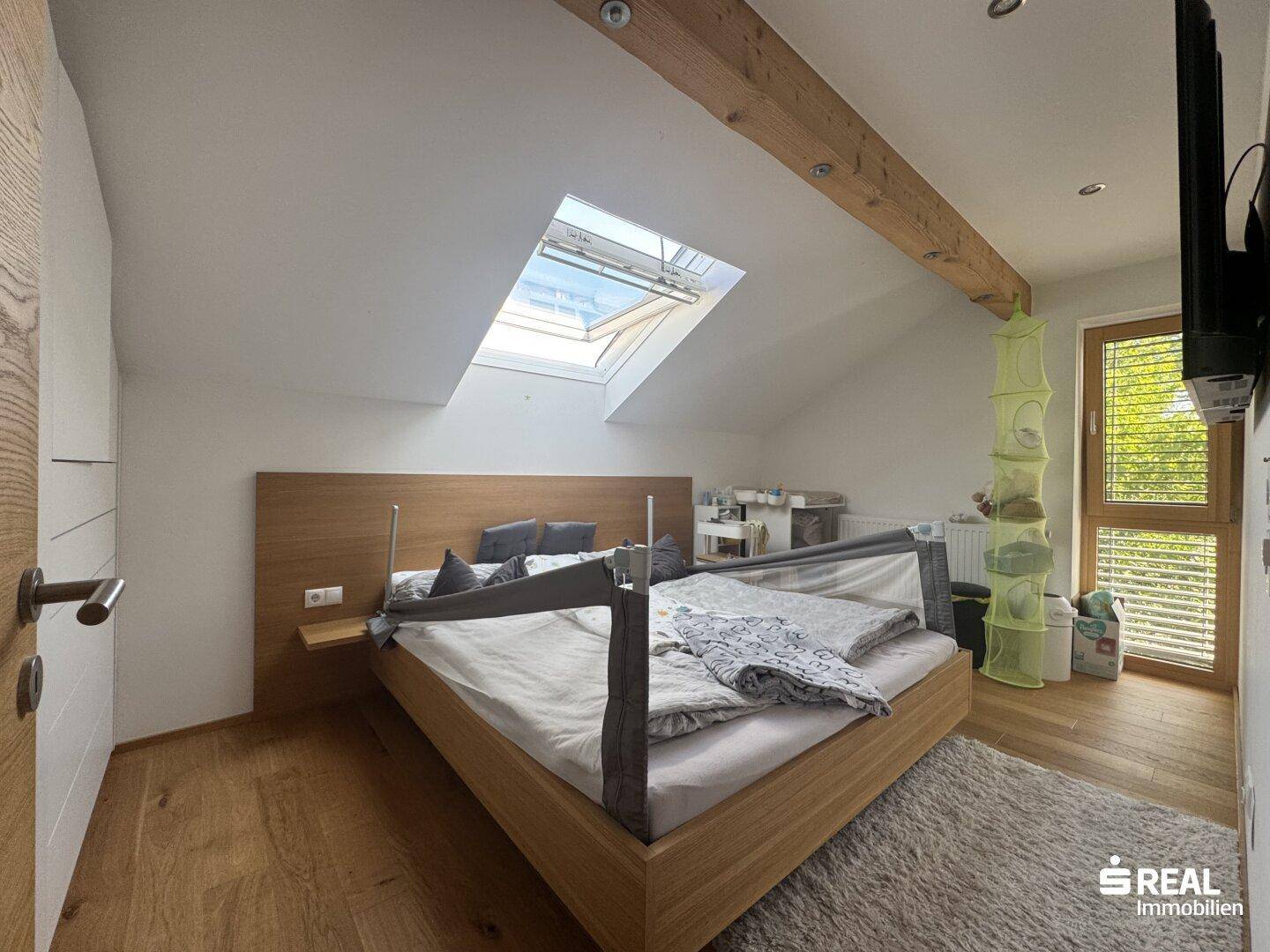 Schlafzimmer im Dachgeschoss mit Holzbett, Holzbalken und Dachfenster für viel Tageslicht.