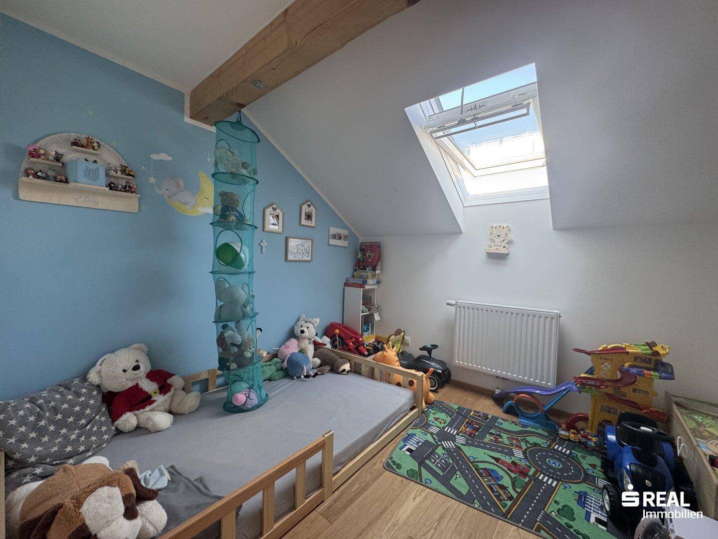 Kinderzimmer im Dachgeschoss mit blau gestrichener Wand, Holzbalken und Dachfenster.