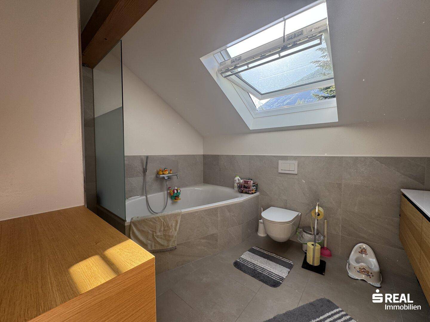Helles Badezimmer mit Badewanne, WC und Dachfenster, das viel Licht hereinlässt.