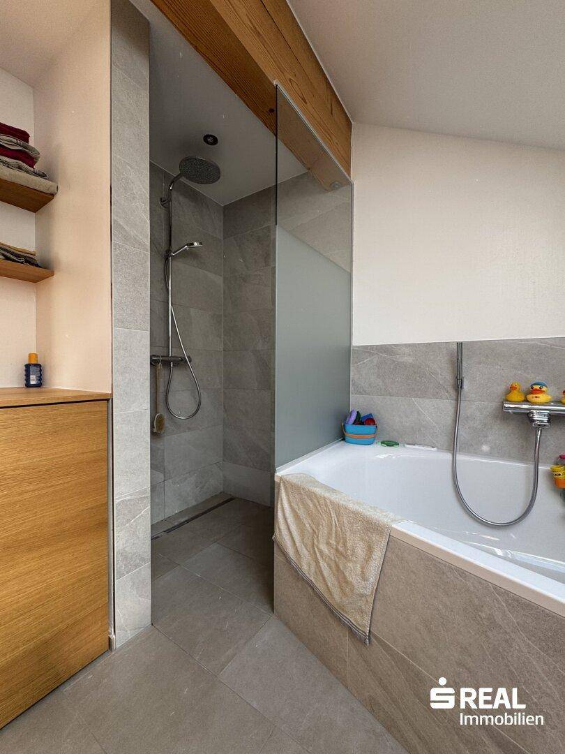 Badezimmer mit begehbarer Dusche und Badewanne, ausgestattet mit modernen Fliesen.
