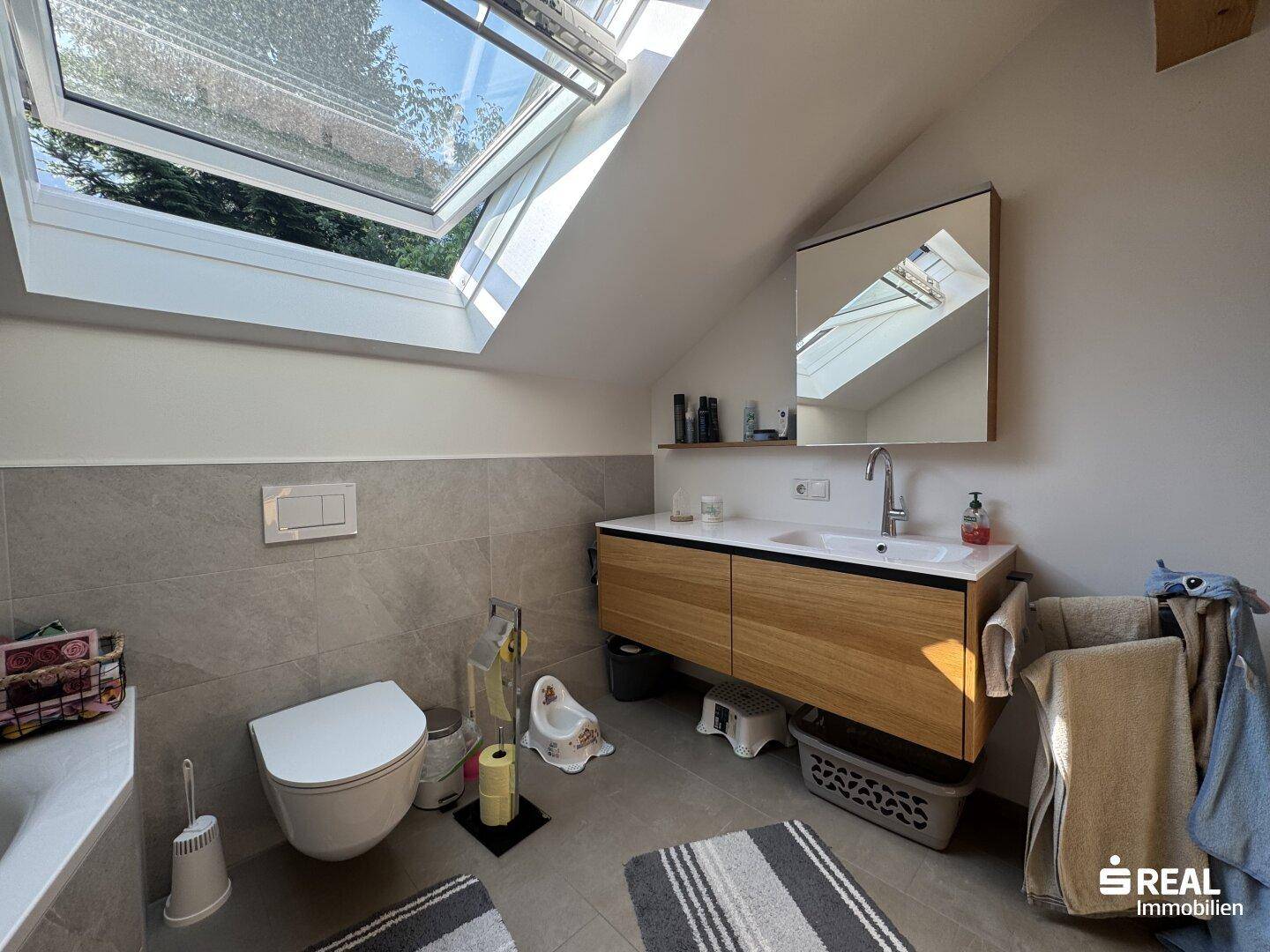 Modernes Badezimmer im Dachgeschoss mit Waschtisch, WC und Dachfenster.