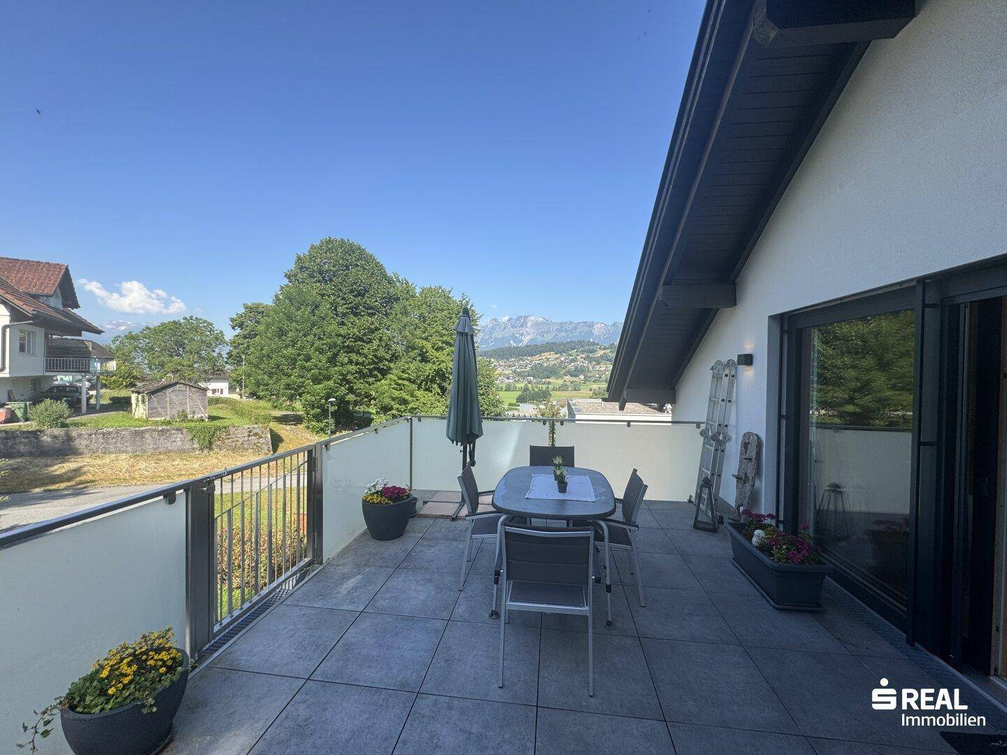 Großer Balkon mit Esstisch und Stühlen, bietet einen weiten Blick auf die Berge.