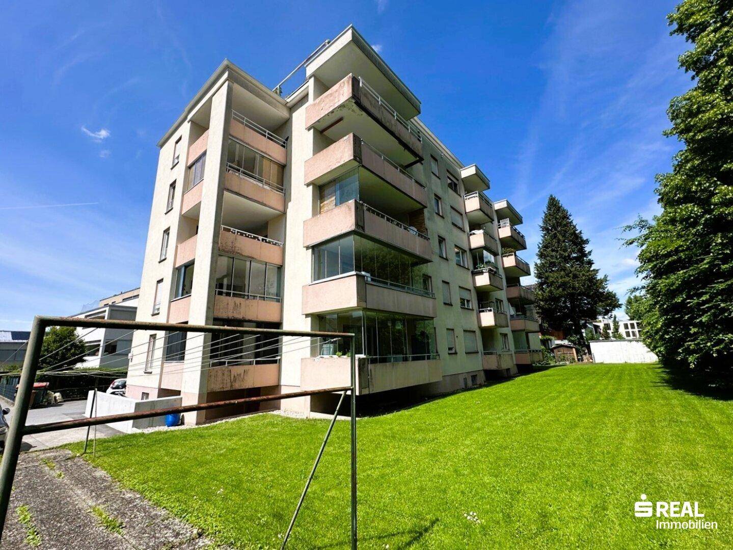 Seitenansicht des Apartmentgebäudes mit mehreren Balkonen und einer gepflegten Grünfläche.