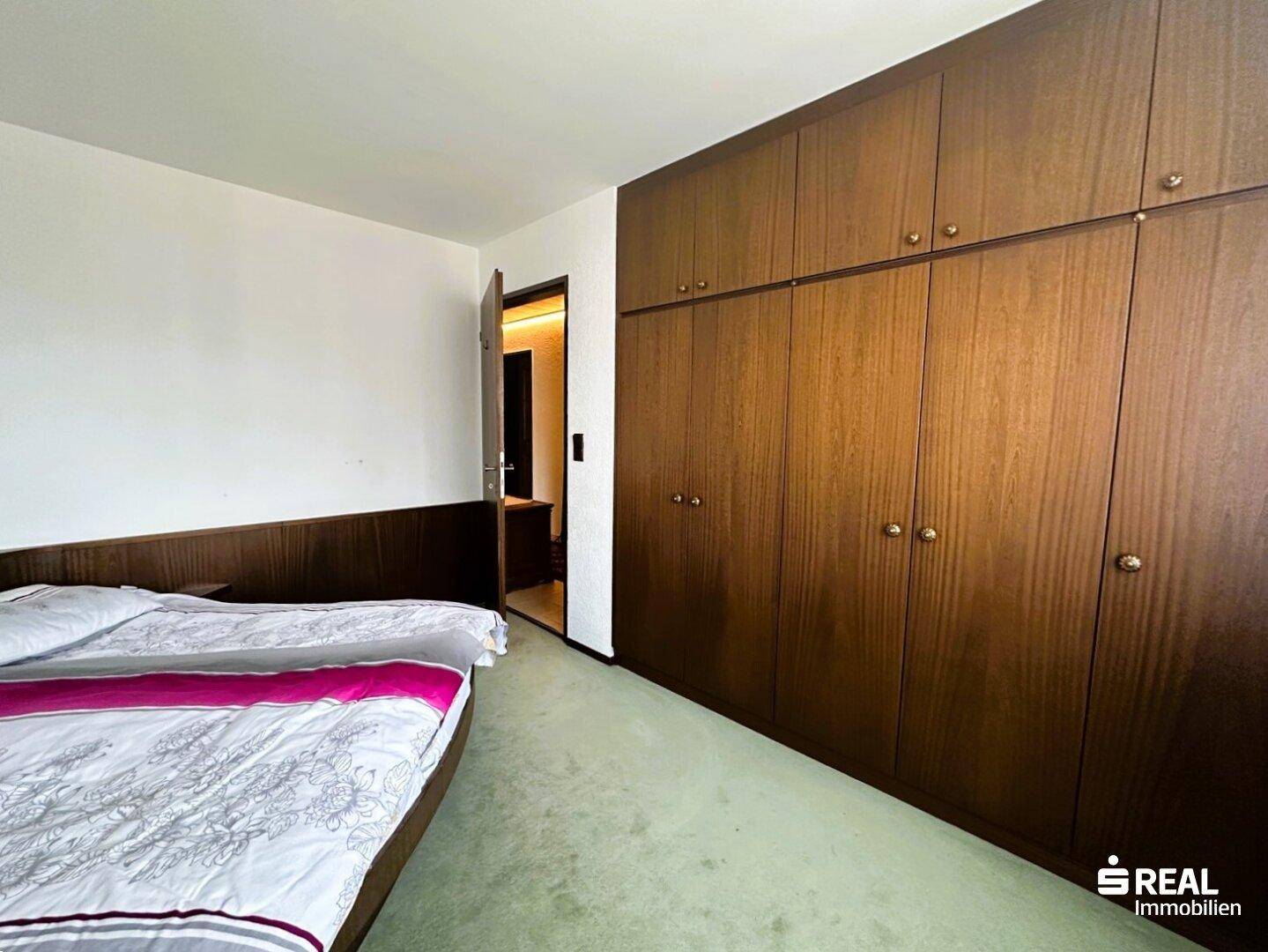 Schlafzimmer mit großen, eingebauten Holzschränken und einem weichen grünen Teppichboden.