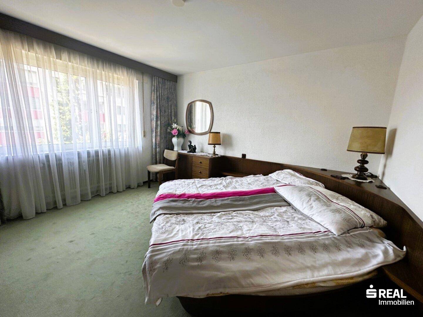 Geräumiges Schlafzimmer mit großem Bett, grünem Teppichboden und Fenstern, die viel Tageslicht hereinlassen.
