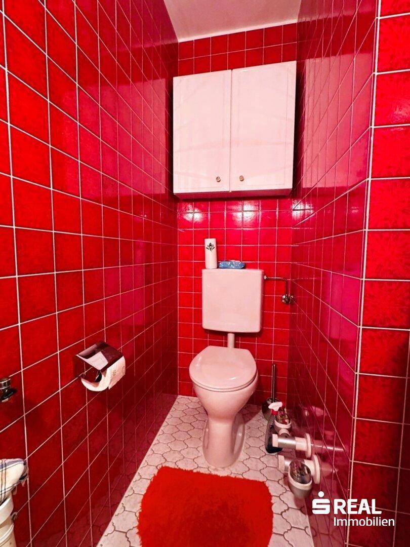 Kleines WC mit auffälligen roten Fliesen an Wänden und Boden, ausgestattet mit einer weißen Toilette.