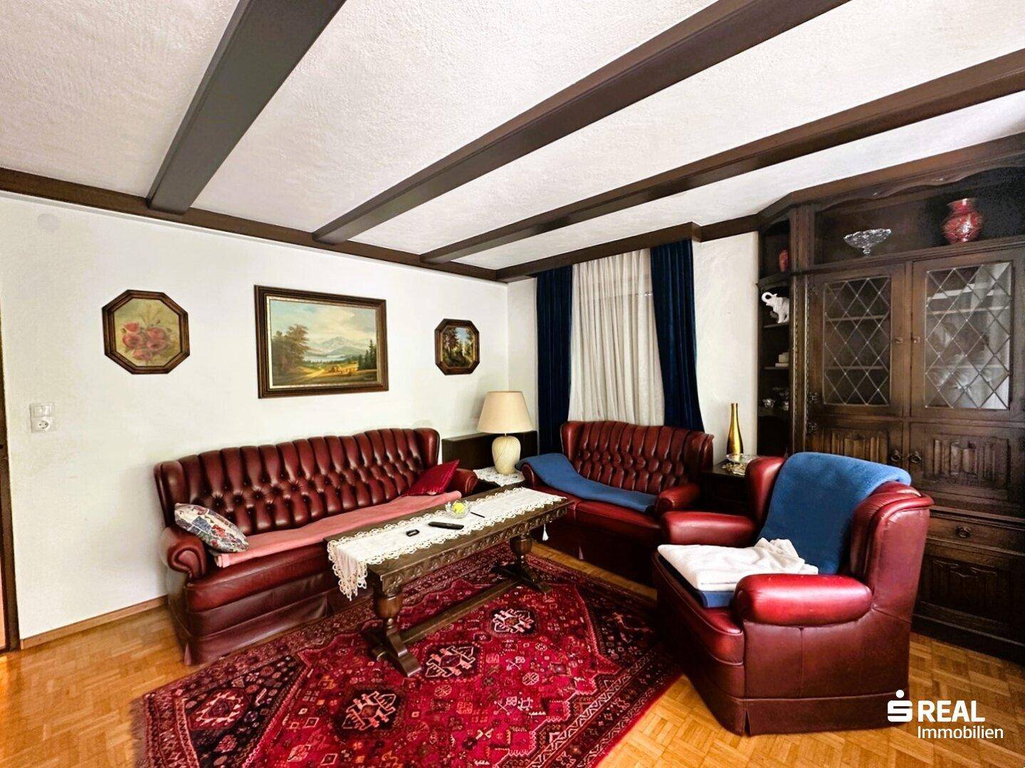 Wohnzimmer mit zwei roten Ledersofas, einem Sessel, Couchtisch und einem traditionellen Holzschrank.