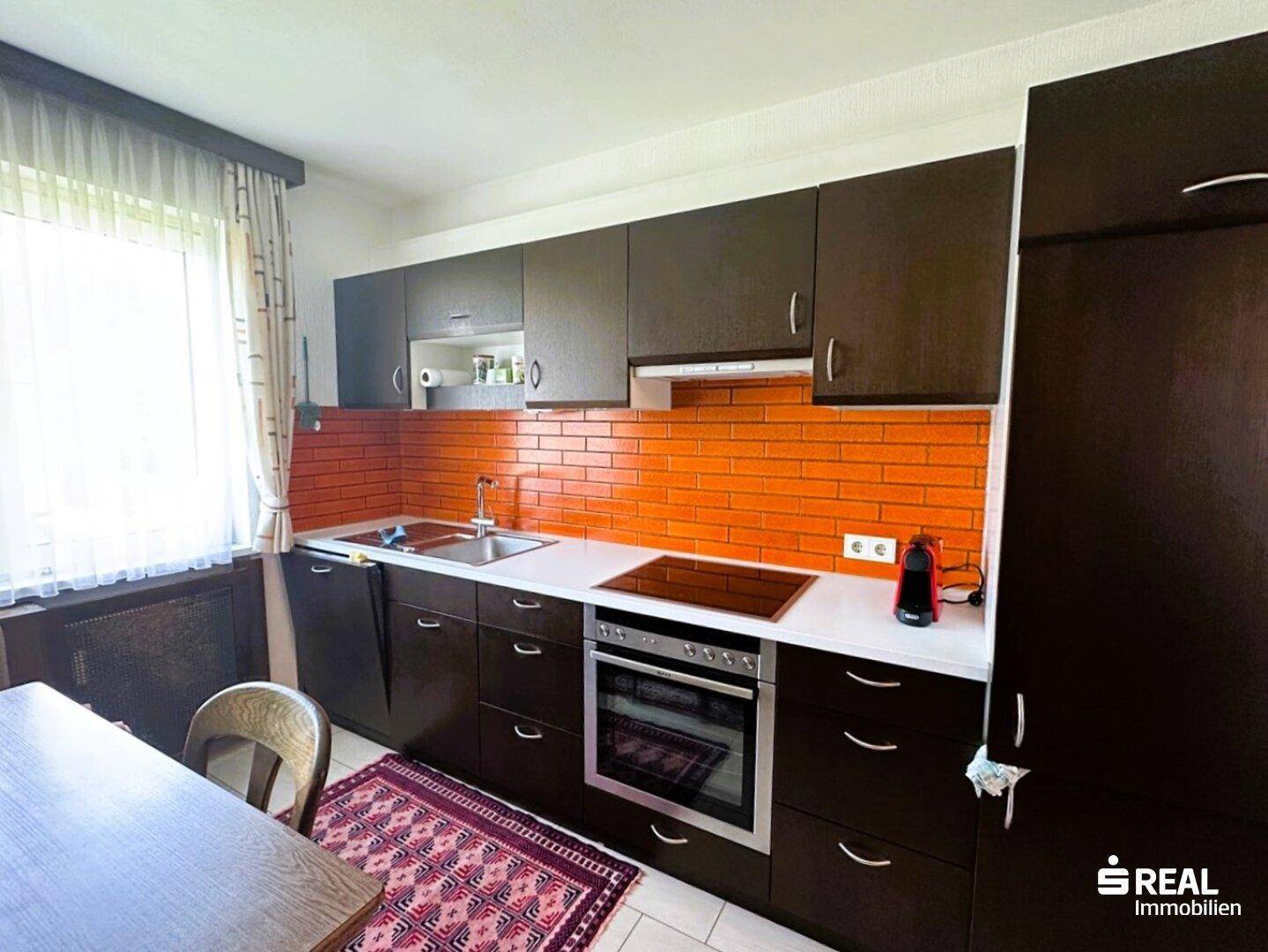 Küche mit dunklen Holzschränken, orangefarbenem Fliesenspiegel und integriertem Backofen und Induktionskochfeld.