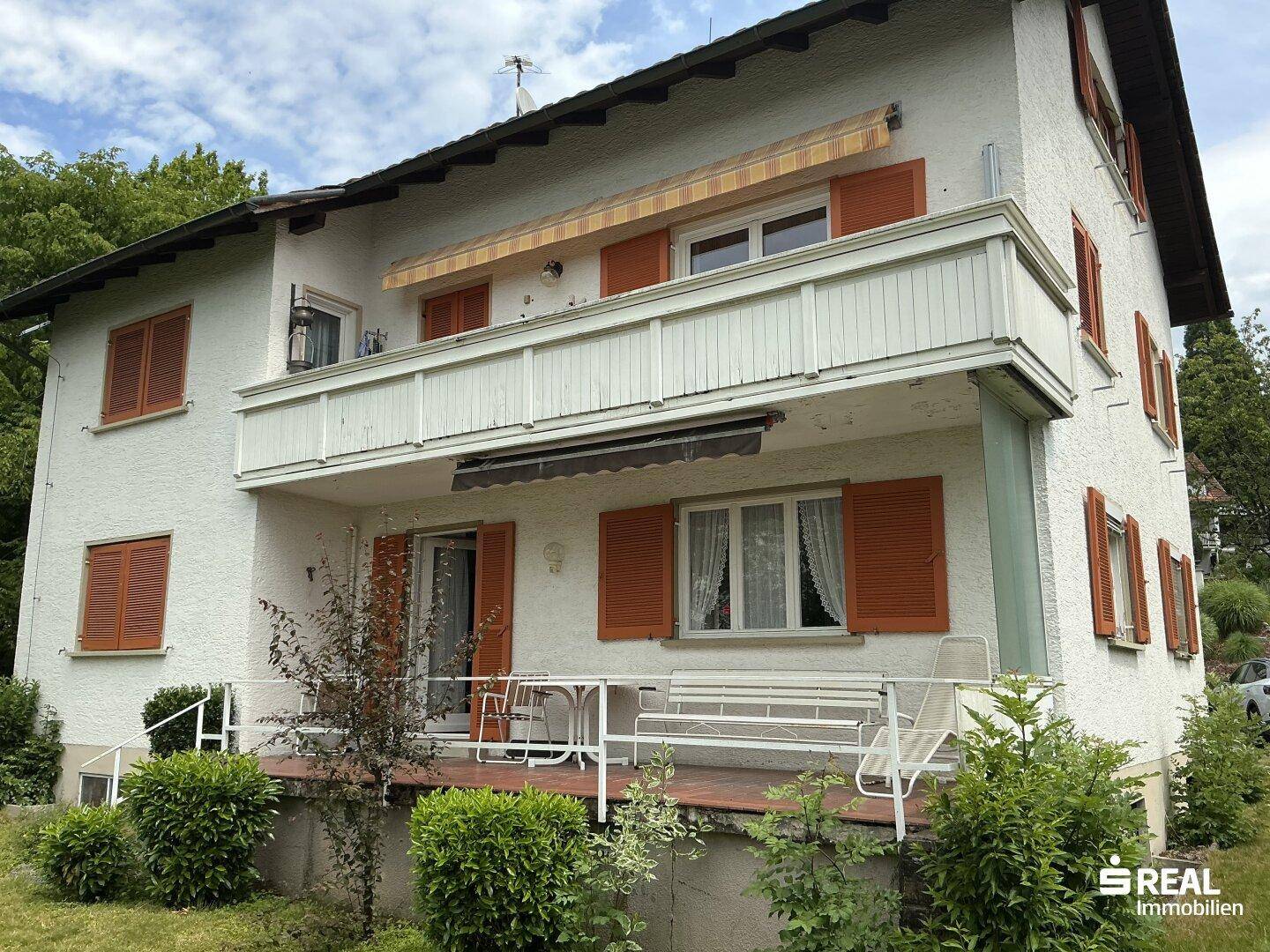 Rückseite des Hauses mit großem Balkon, Markise und einer Terrasse mit Gartenmöbeln.