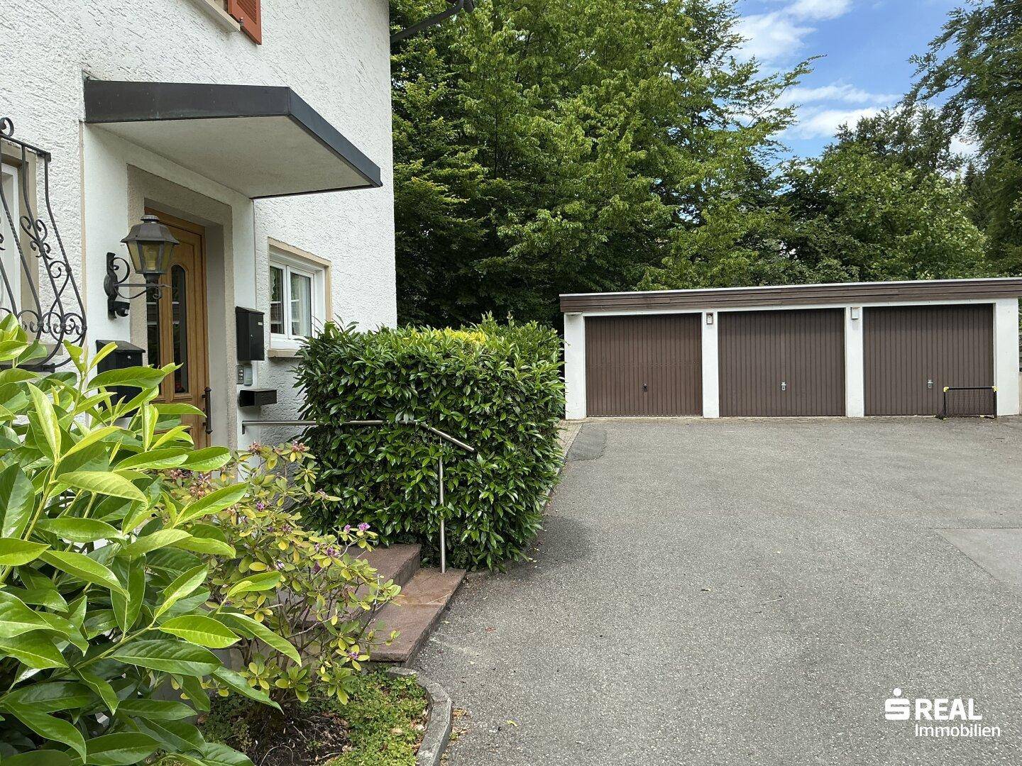 Eingangsbereich des Hauses mit gepflegter Hecke und drei Garagen im Hintergrund.