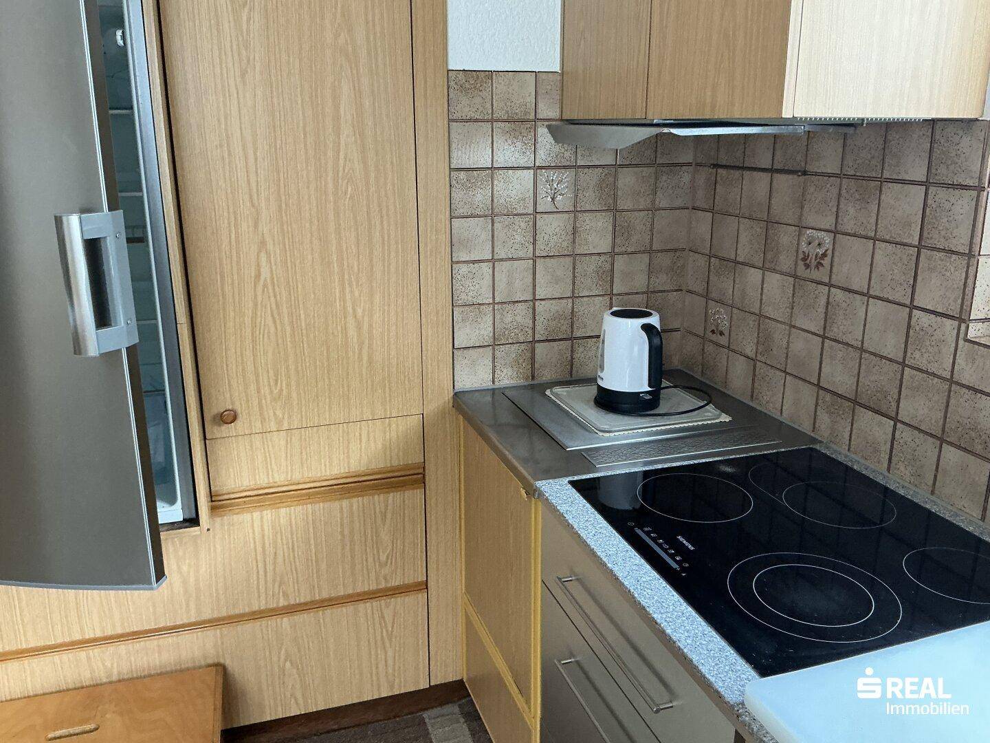 Detailansicht der Küche mit Induktionskochfeld, Dunstabzugshaube und Kühlschrank.