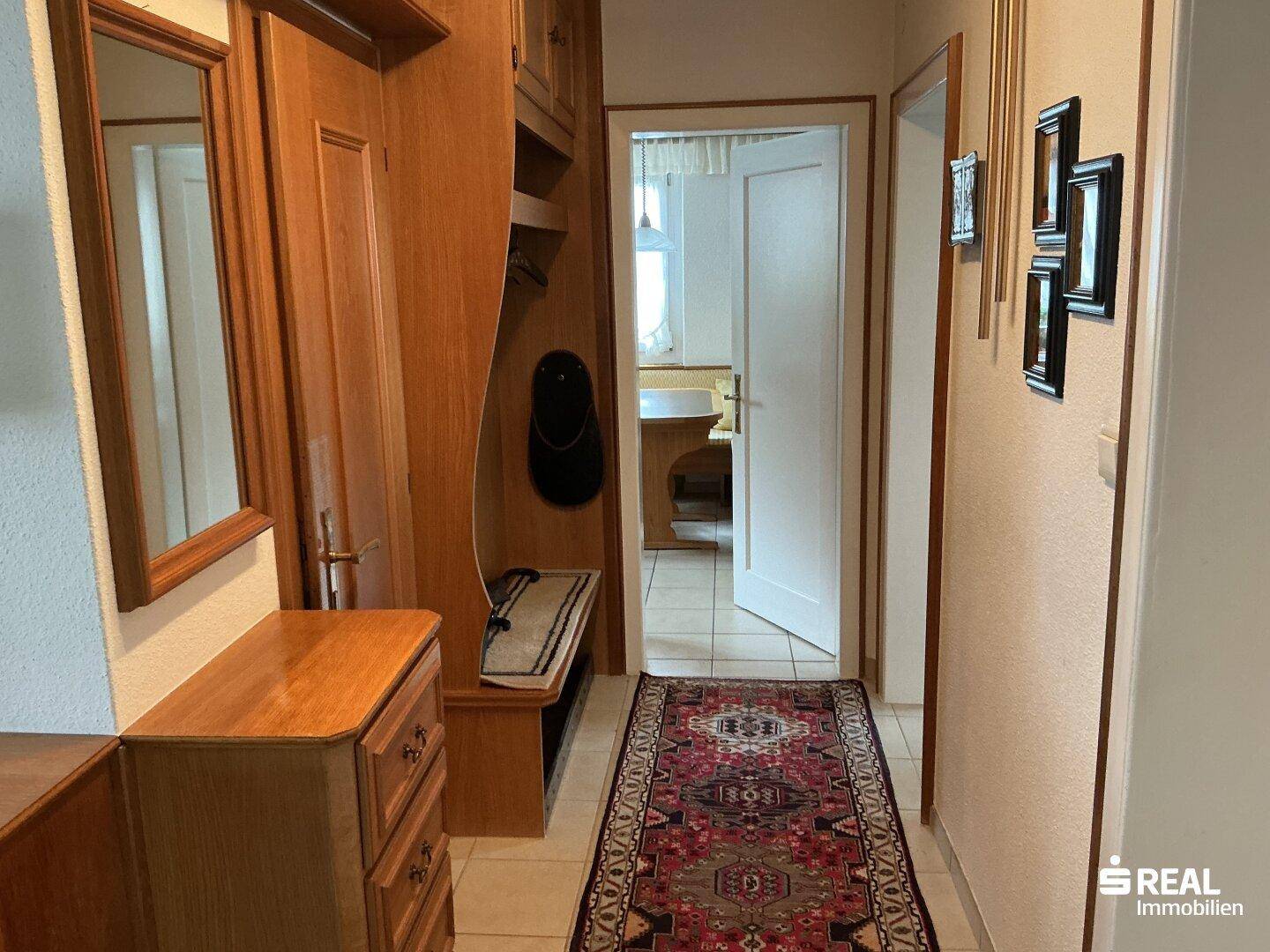 Eingangsbereich mit Garderobe aus Holz, Spiegel und einem Teppich auf Fliesenboden.