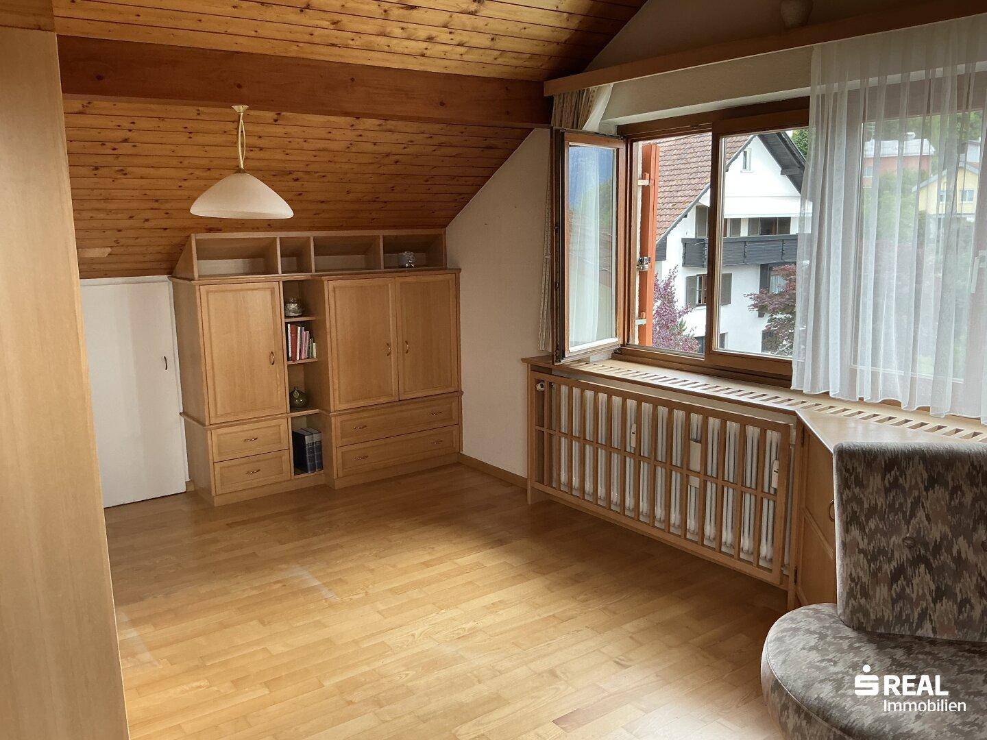 Dachzimmer mit Holzdecke, Parkettboden und einem großen Fenster, ausgestattet mit Einbauschränken.