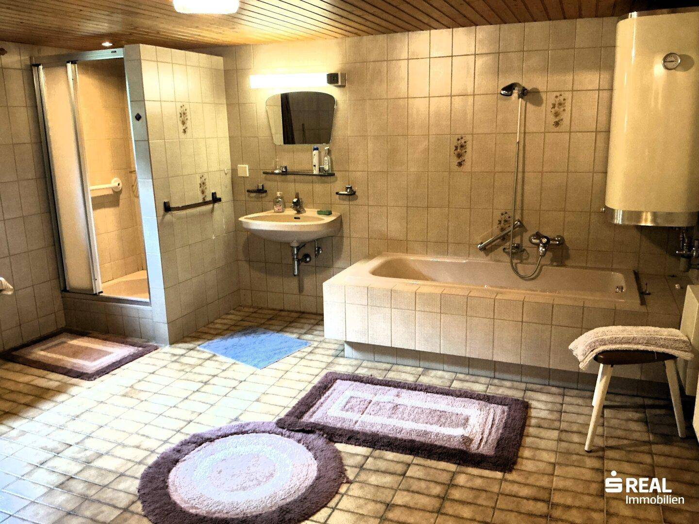 Geräumiges Badezimmer mit Badewanne, Duschkabine und Waschbecken, komplett gefliest.