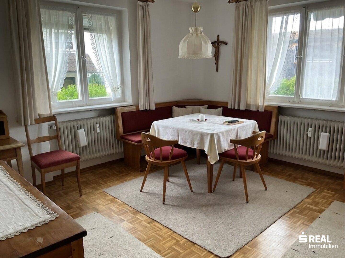 Traditioneller Essbereich mit Eckbank, Holztisch und Stühlen, umgeben von Fenstern und Parkettboden.