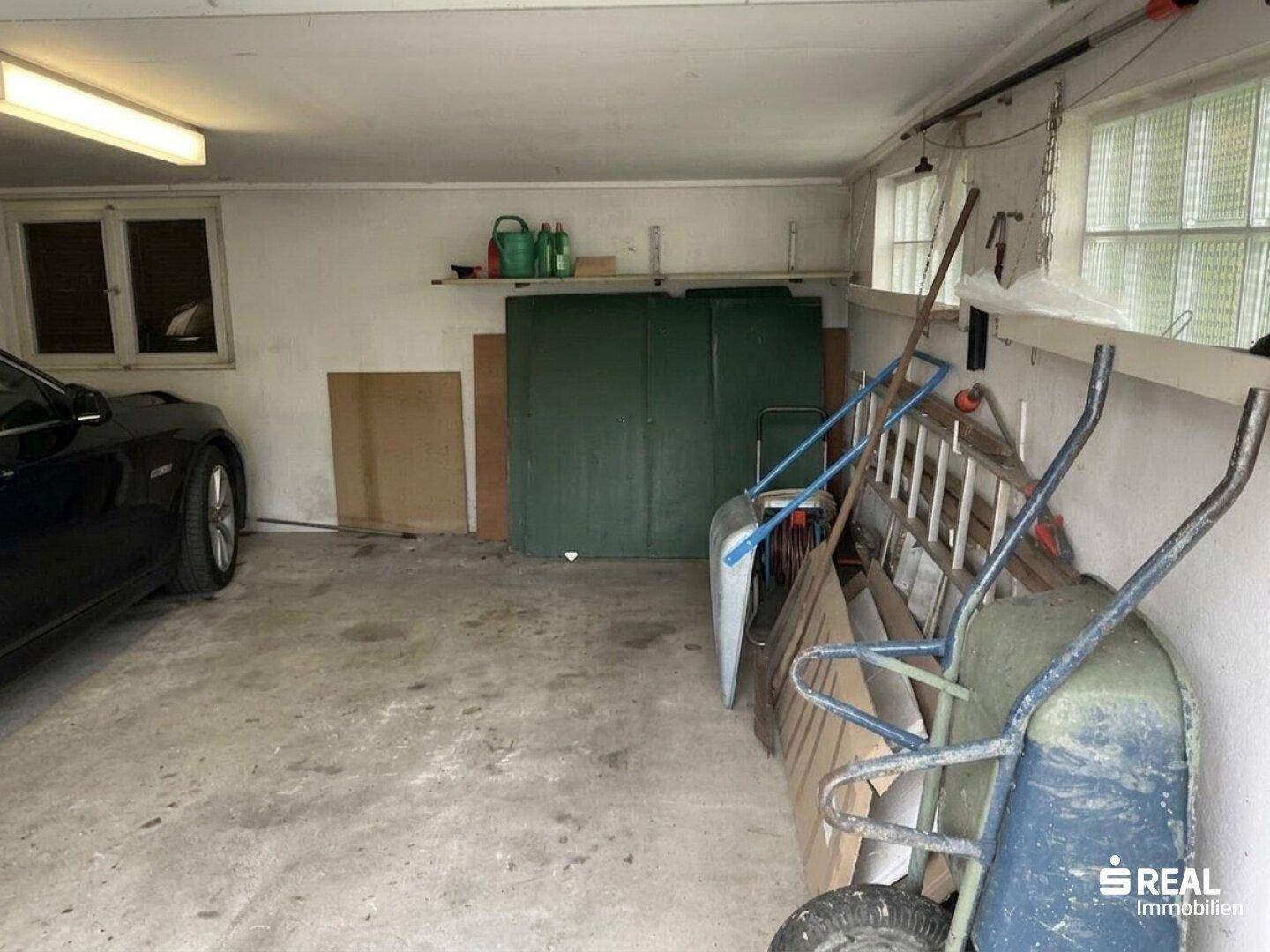 Geräumige Garage mit Betonboden, Fenster und Abstellmöglichkeiten für Werkzeuge.