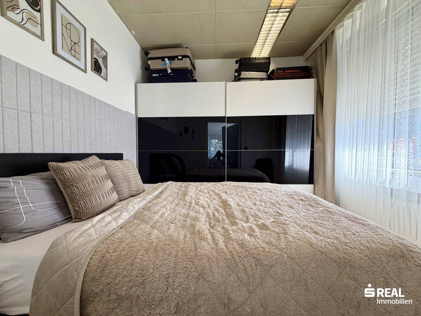 Schlafzimmer mit großem Bett, modernem Kleiderschrank und Fenster mit Vorhängen.