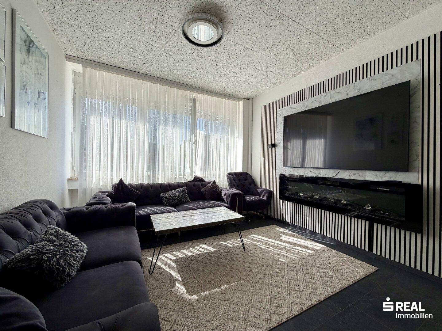 Gemütliches Wohnzimmer mit großer Couch, modernem TV-Bereich und viel Tageslicht durch große Fenster.