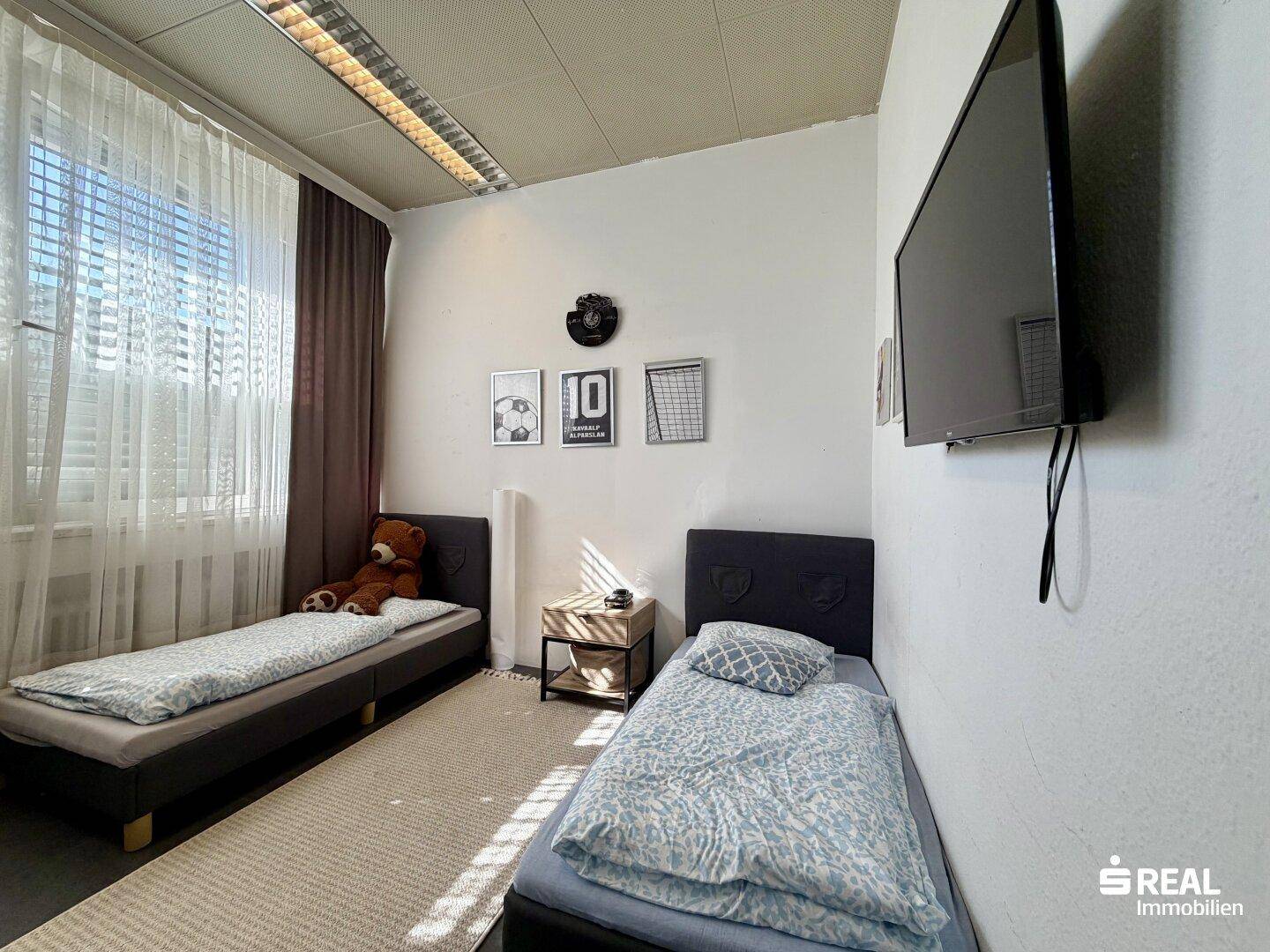 Kinder- oder Gästezimmer mit zwei Einzelbetten, kleinem Nachttisch und Wandfernseher.
