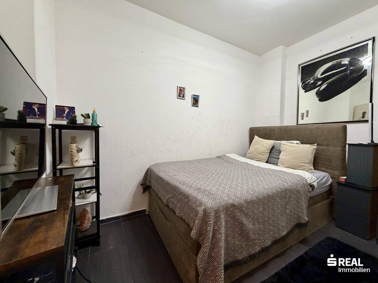 Gemütliches Schlafzimmer mit Doppelbett, Schreibtisch und dunklem Boden, dekoriert mit Kunstwerken.