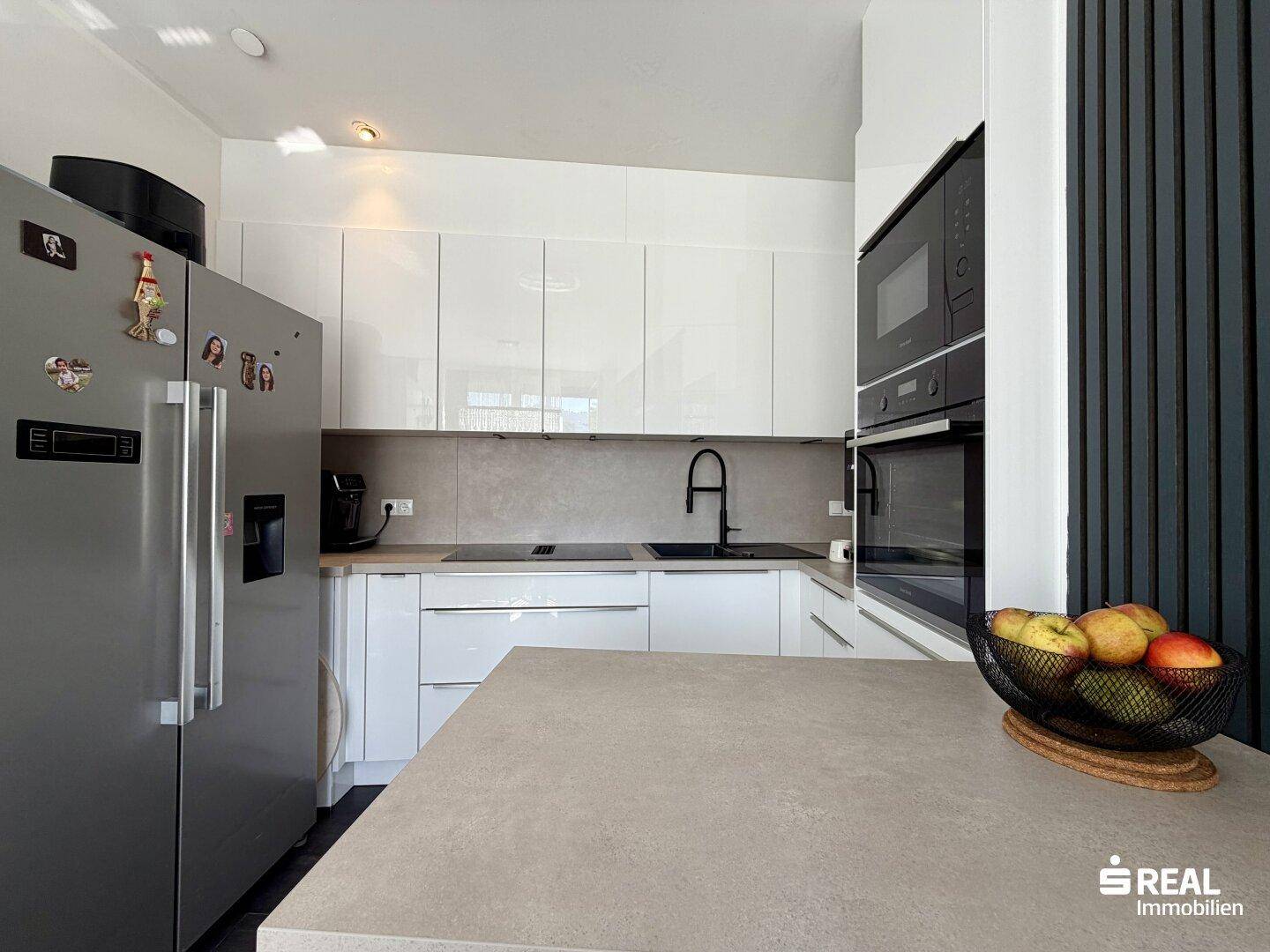 Moderne Küche mit weißen Hochglanzschränken, integrierten Geräten und großem Kühlschrank.