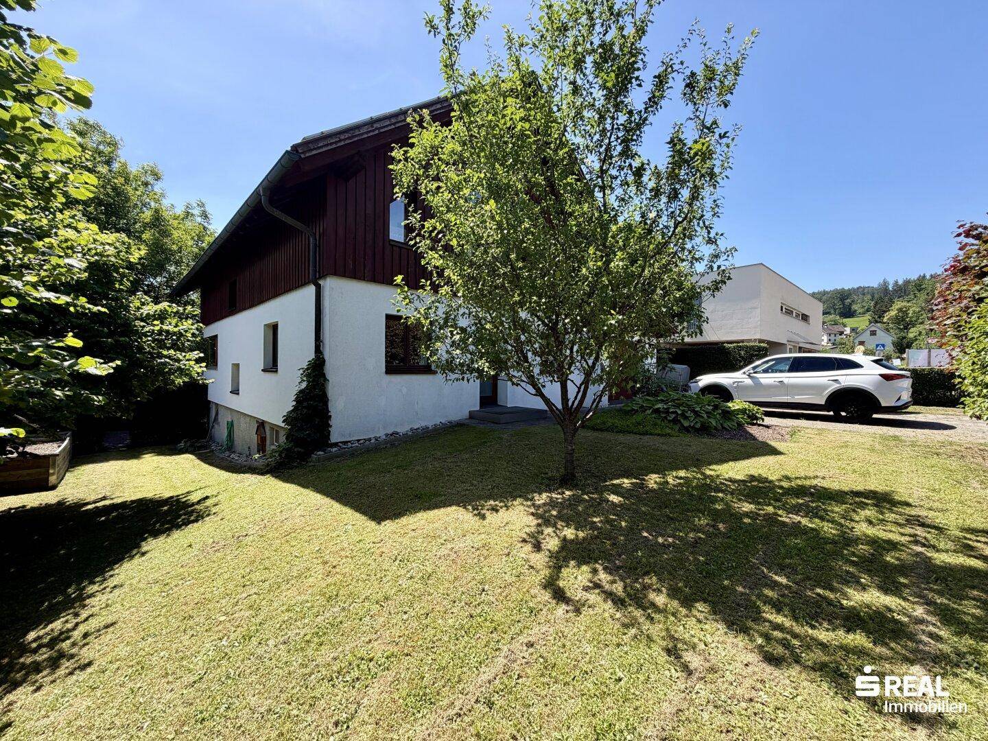 Charmantes Einfamilienhaus mit gepflegtem Rasen und altem Baumbestand an einem sonnigen Tag.