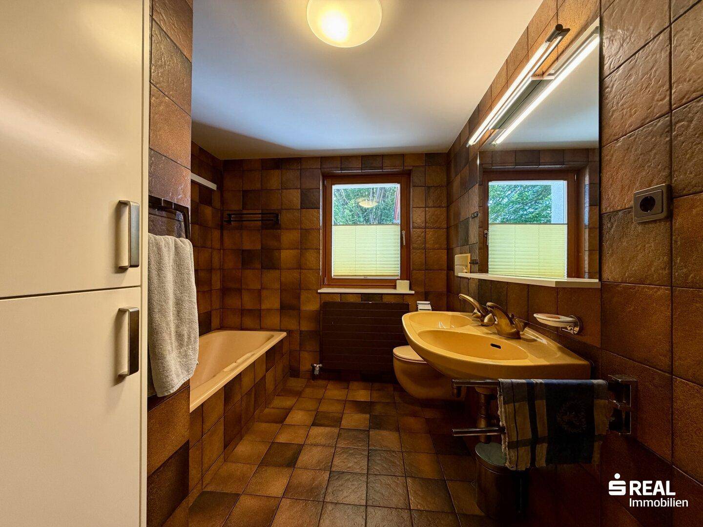 Badezimmer im Stil der 80er Jahre mit braunen Fliesen, Badewanne und Doppelwaschbecken.