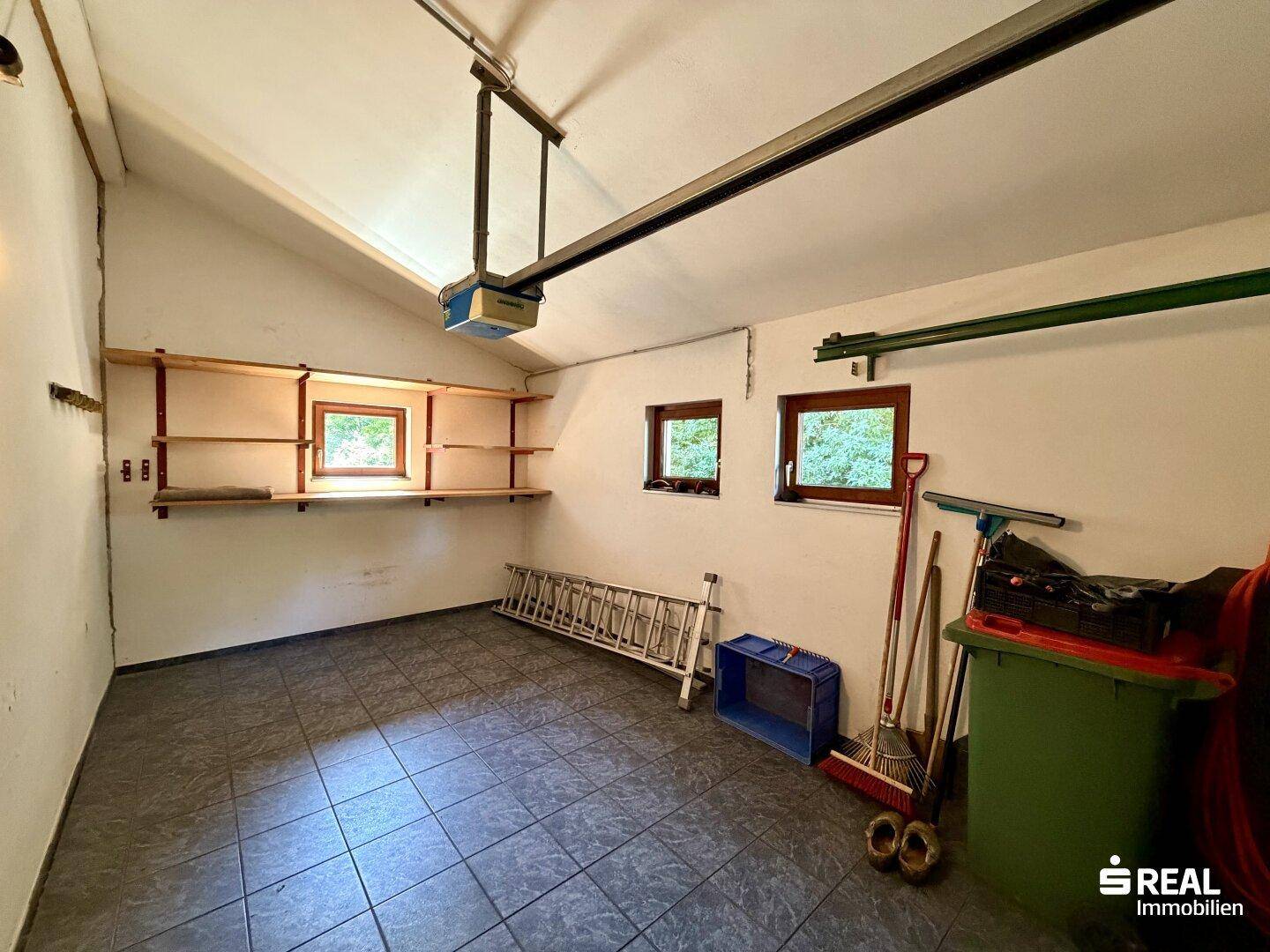 Geräumige Garage mit Fliesenboden, Regalen und Fenstern für Tageslicht.