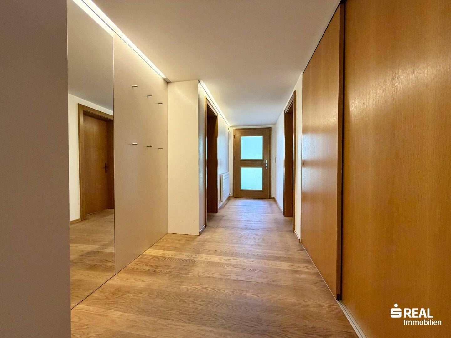 Heller Flur mit Holzboden und integrierten Schränken, der zu weiteren Räumen führt.