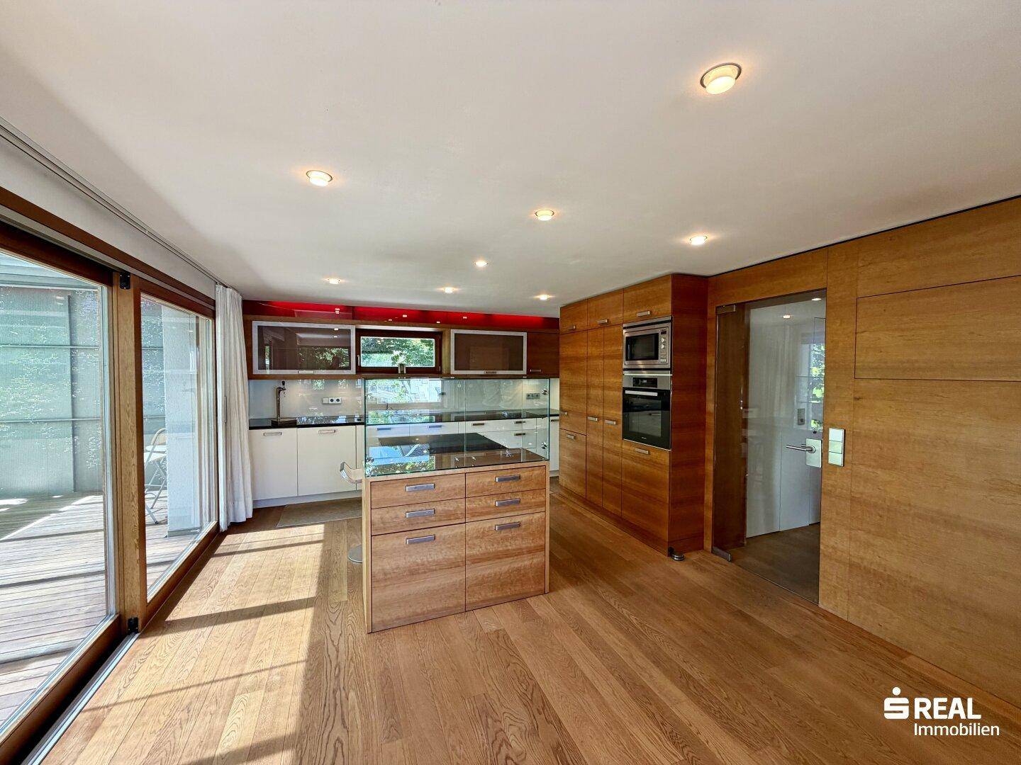 Moderne offene Küche mit Holzboden, integrierten Geräten und Zugang zur Terrasse.