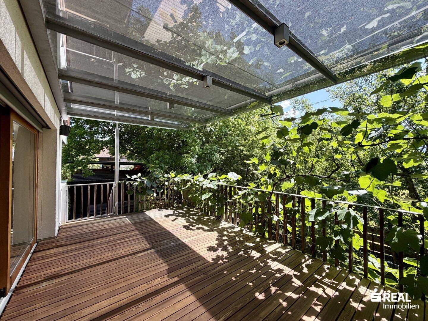 Geräumiger überdachter Balkon mit Holzboden und Blick ins Grüne, ideal zum Entspannen.
