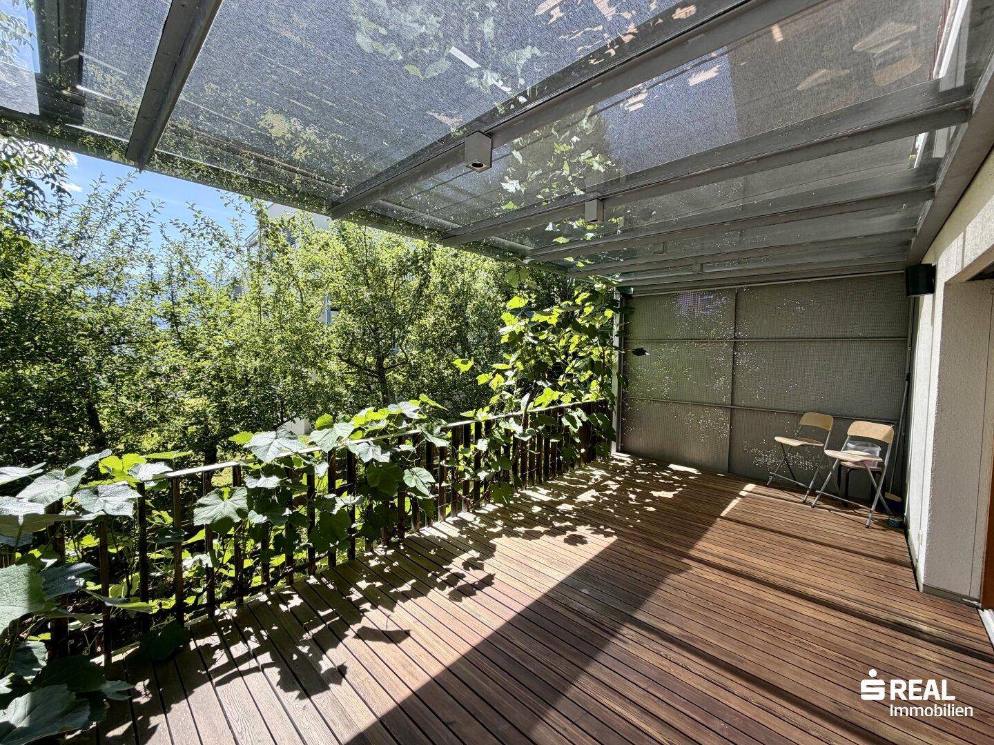 Überdachte Holzterrasse mit üppiger Begrünung, ideal für entspannte Stunden im Freien.