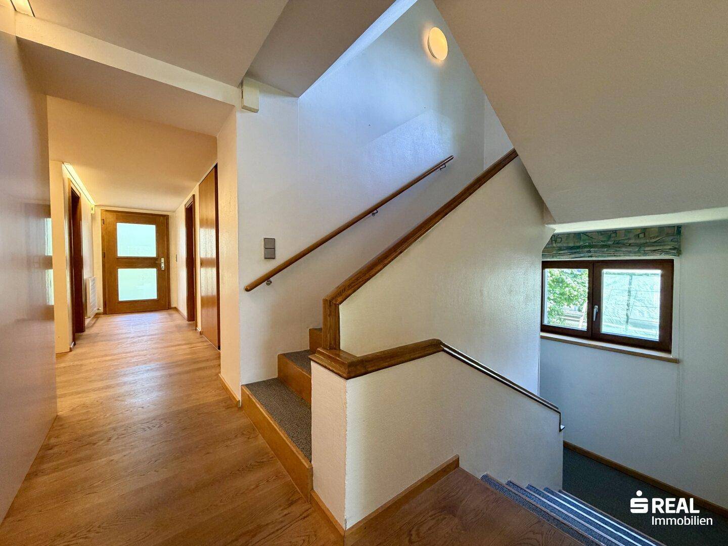 Heller Flur mit Holztreppe, Holzgeländer und Zugang zu weiteren Räumen.