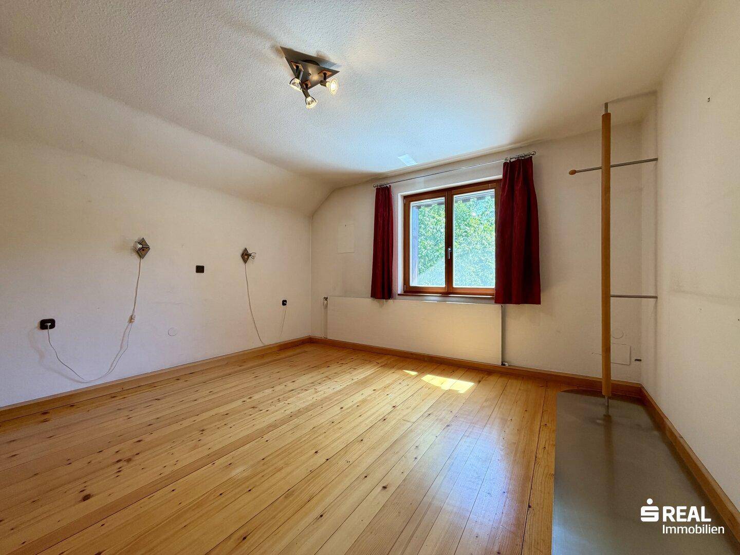 Geräumiges Schlafzimmer mit Holzdielenboden, weiß gestrichenen Wänden und Fensterblick.