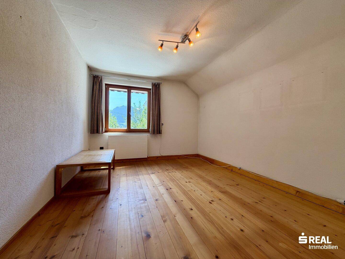 Helles Schlafzimmer mit Holzdielenboden, einfacher Einrichtung und Fenster mit Bergblick.