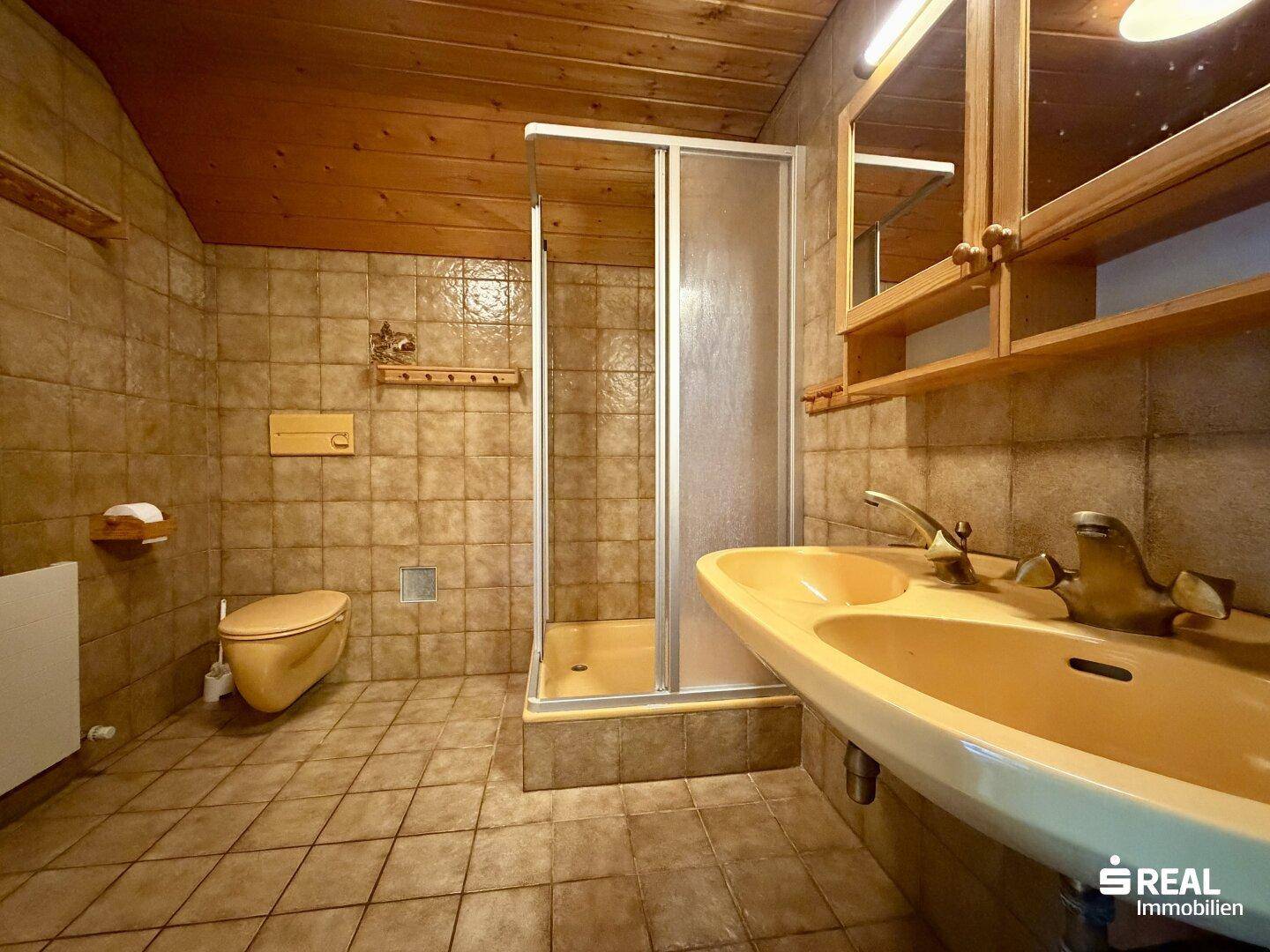Badezimmer im Stil der 80er Jahre mit braunen Fliesen, Dusche und Einzelwaschbecken.