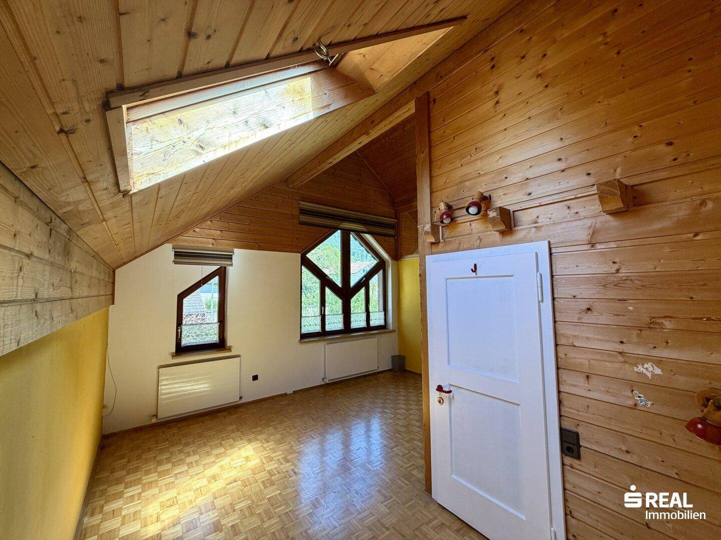Gemütliches Zimmer im Dachgeschoss mit Holzverkleidung, Dachfenster und schrägen Wänden.