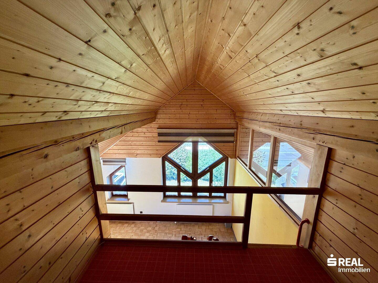 Offener Dachbodenbereich mit Holzverkleidung und Blick auf das darunterliegende Zimmer.