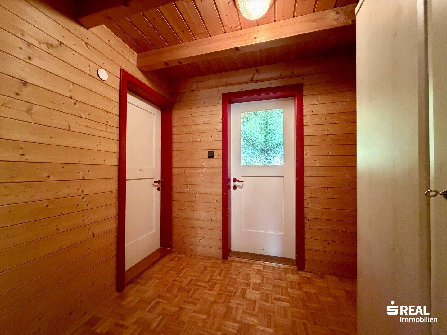 Rustikaler Flur im Dachgeschoss mit Holzvertäfelung und zwei Türen, die zu weiteren Räumen führen.